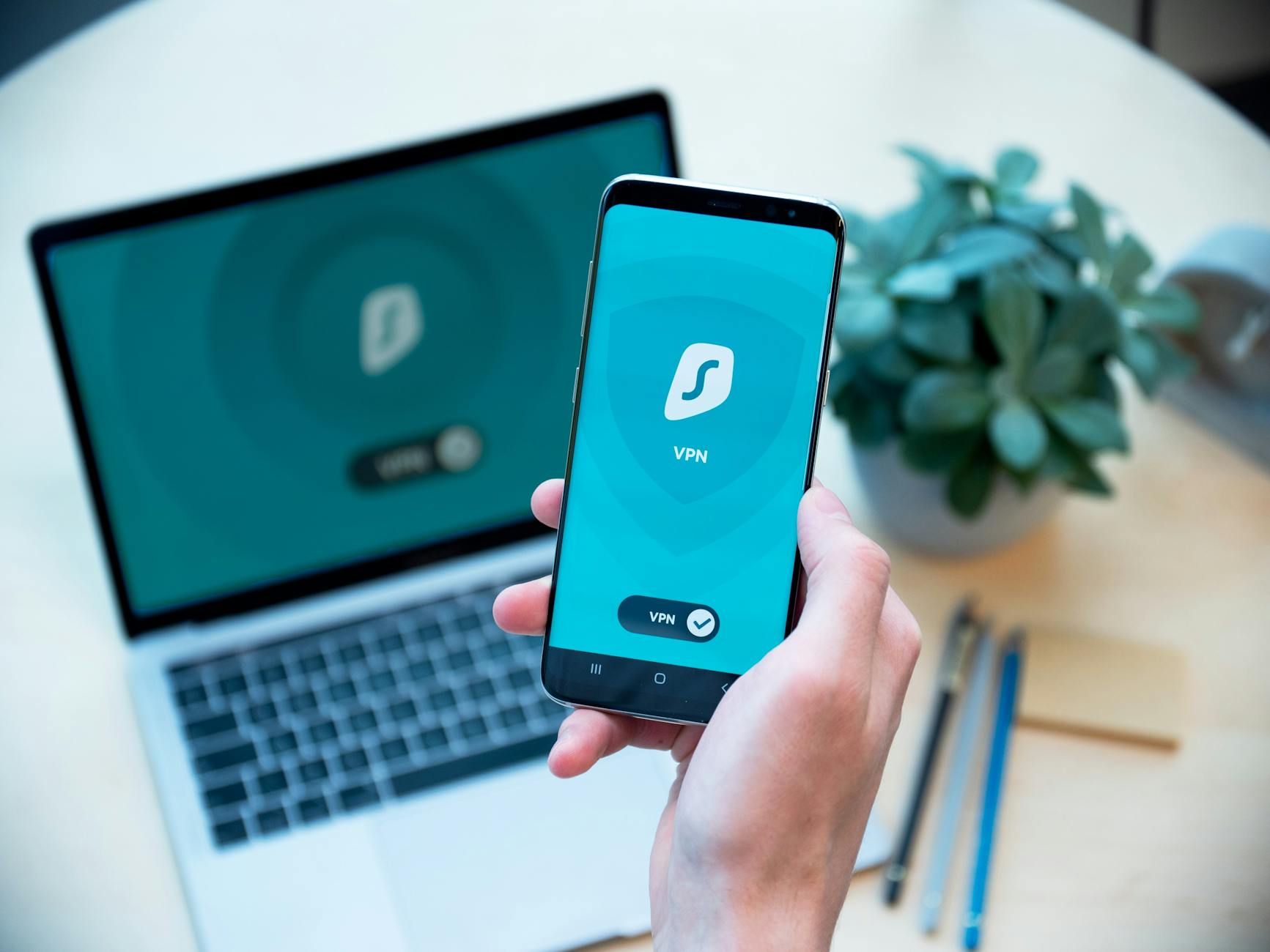 Dłoń trzymająca smartfon z aplikacją VPN na tle laptopa