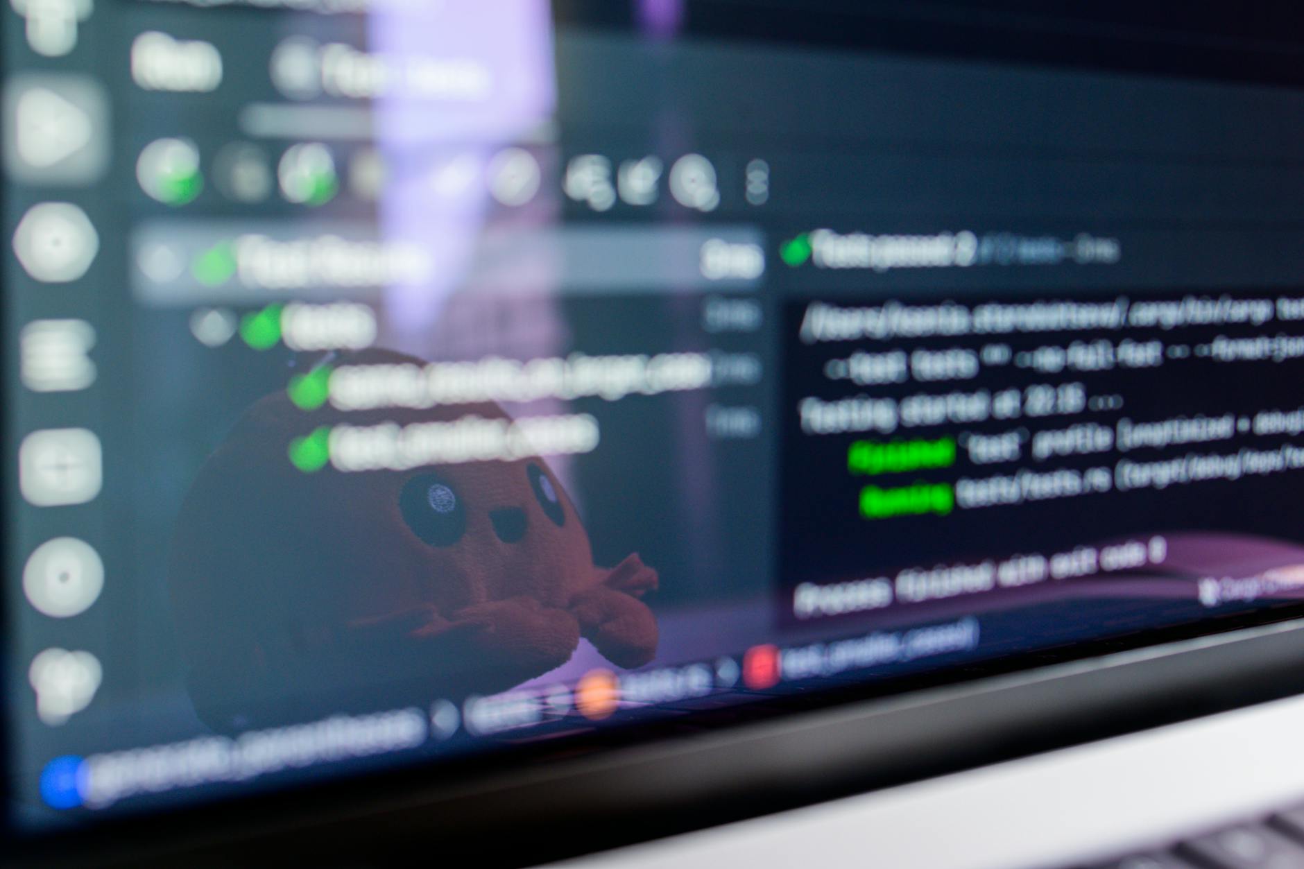 Ekran laptopa z kodem programistycznym i odbiciem pluszowej maskotki