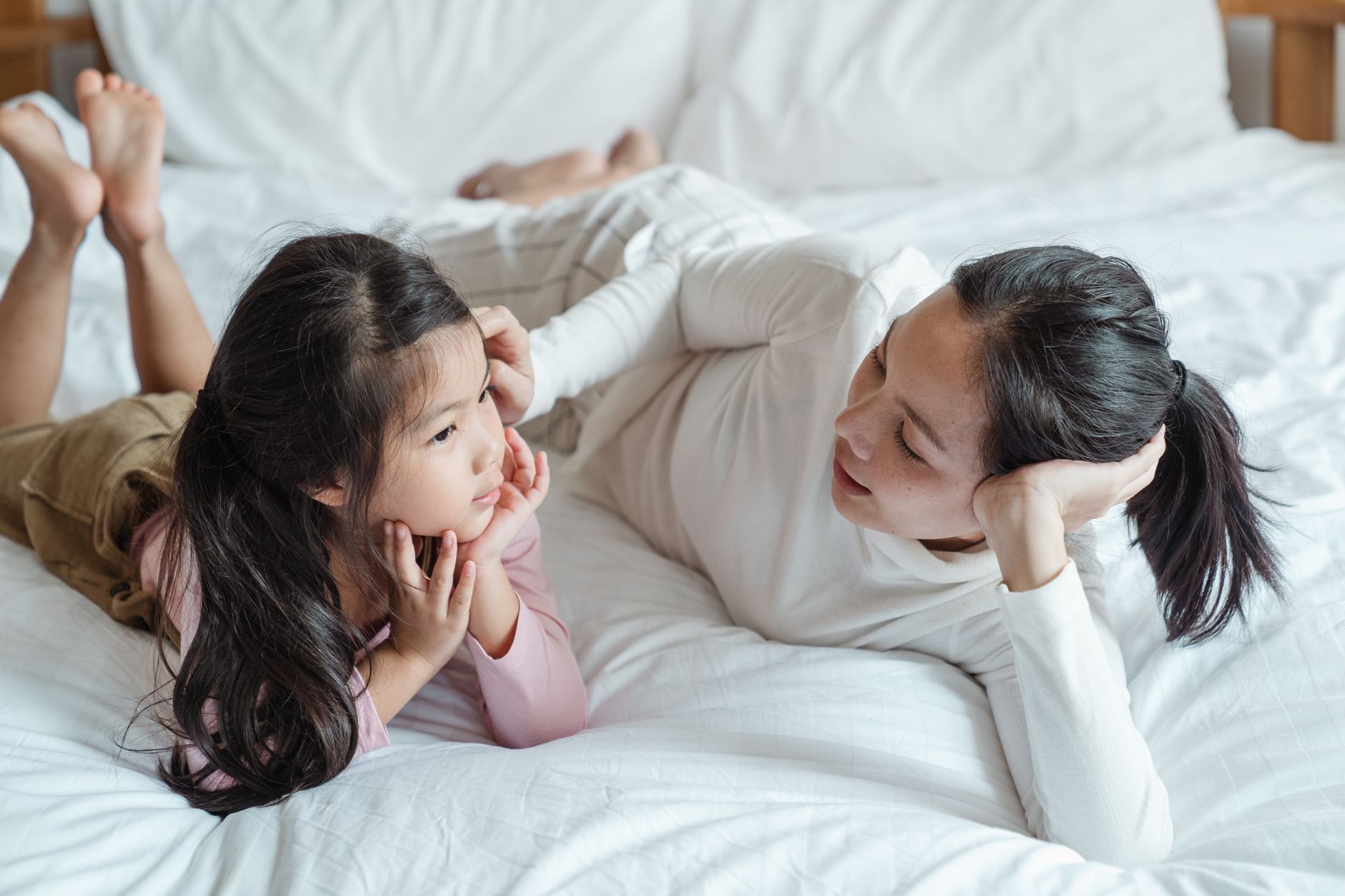 Mama rozmawia z córką na łóżku, spędzając czuły czas razem