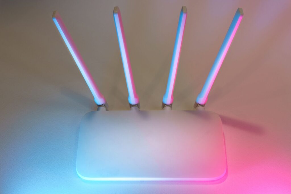 Biały router Wi‑Fi z czterema antenami i niebiesko-różowym podświetleniem